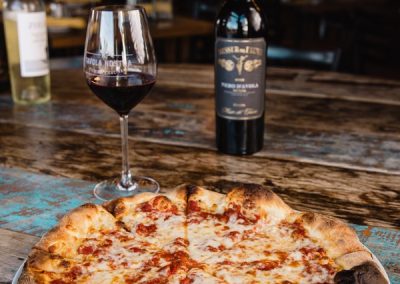 alt=" A cheese pizza displayed on a table with a bottle and cup of wine right next to it"